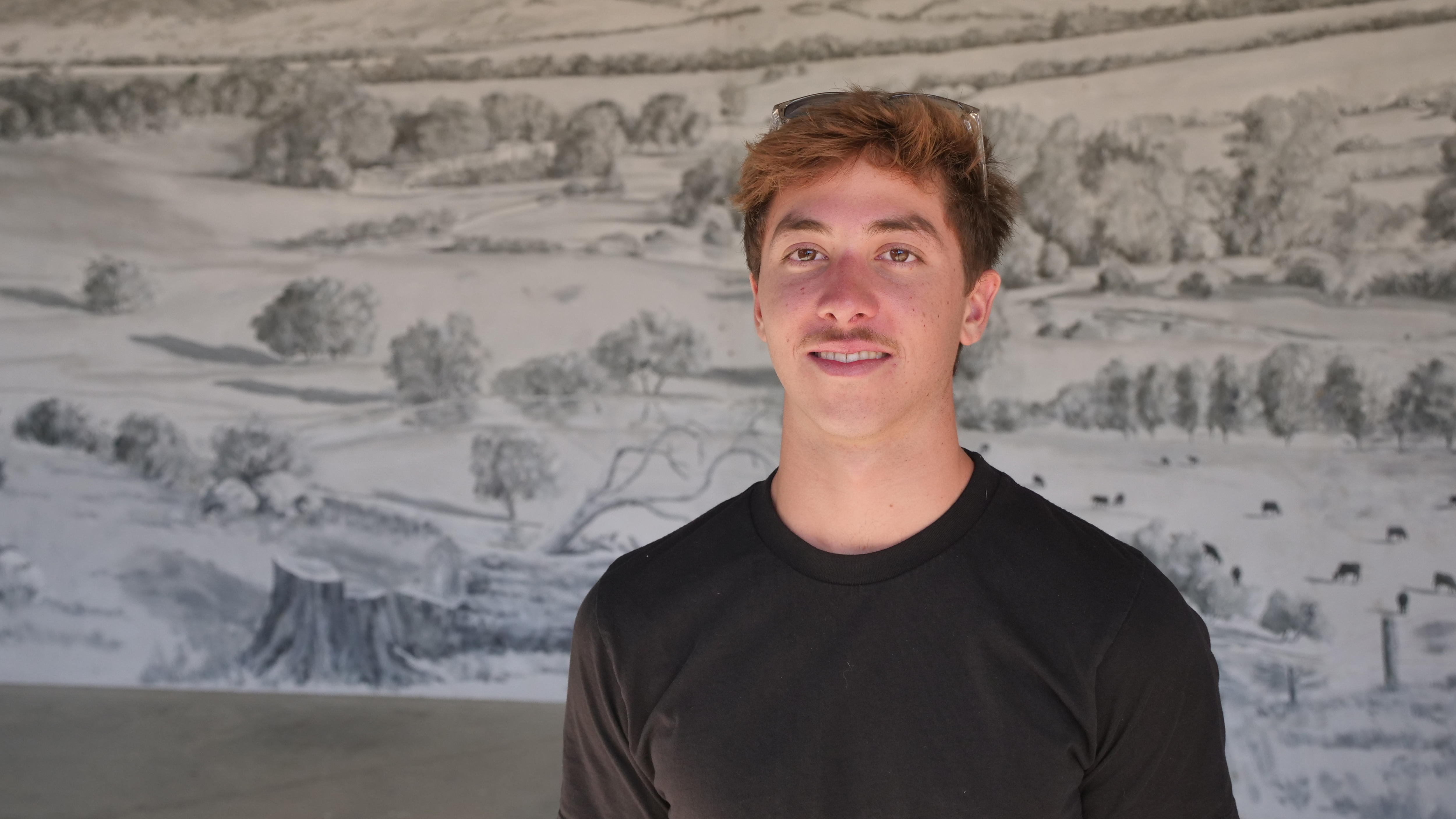 Um jovem olha para a câmera com um mural atrás dele