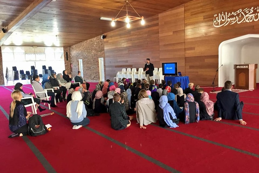 A view of inside the Ahmadiyya mosque where children are sitting listening to a speaker.