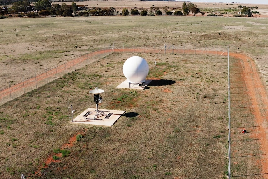 A large, white sphere in a fenced paddock with a smaller satellite in front