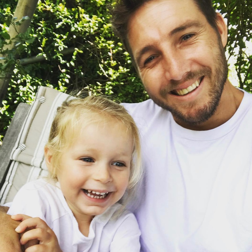 Mr Thomas smiles and hugs Matilda in a deck chair outside. Matilda is laughing.