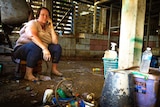 Kirsty MacGregor talks on her phone while sitting on a crate, on a muddy floor, surrounded by objectes caked in mud.