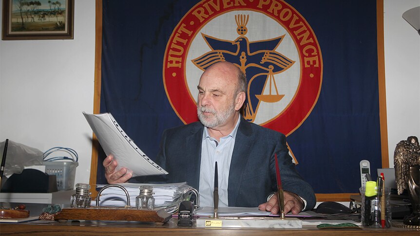 Prince Graeme sitting in front of a Hutt River Province banner and examining some paperwork.