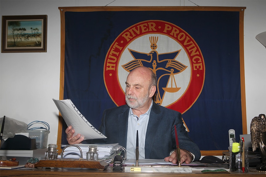 Prince Graeme sitting in front of a Hutt River Province banner and examining some paperwork.