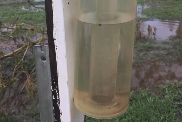 A half full rain gauge in the foreground with a flooded paddock in the background