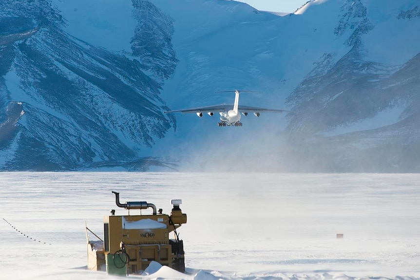 A vehicle drives across a polar landscape as a plane flies overhead