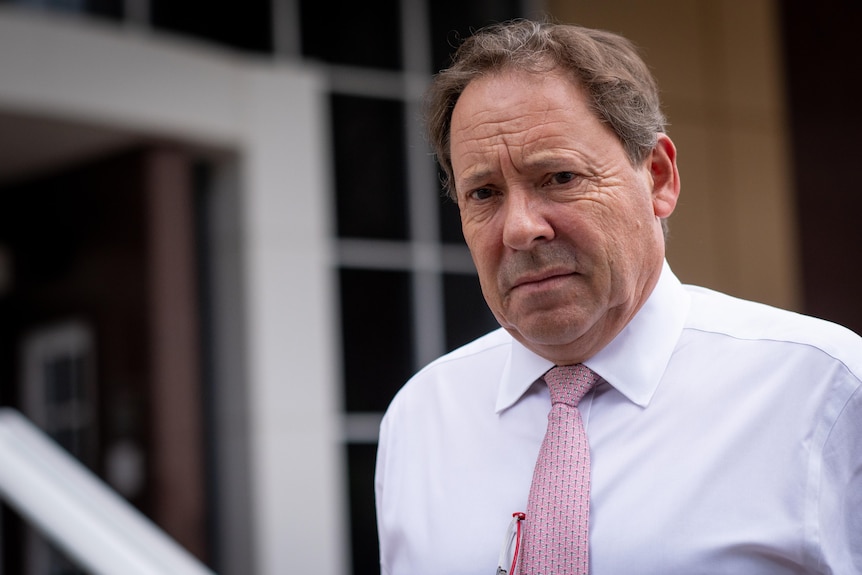 A man with a white shirt and pie tie can be seen outside the NT Supreme Court. He looks serious.