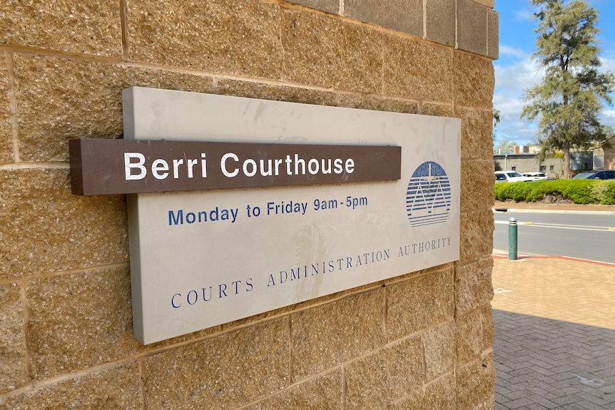 A sign on a sandy stone brick wall, which reads Berri Courthouse. Next to the wall, the sky is blue and cloudy. 