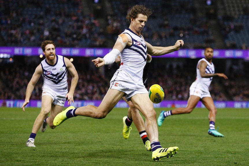 Nat Fyfe kicks the ball, teammates run behind him.