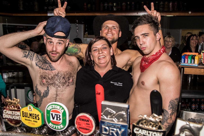 Three shirtless male bartenders with a female bar manager behind the bar.