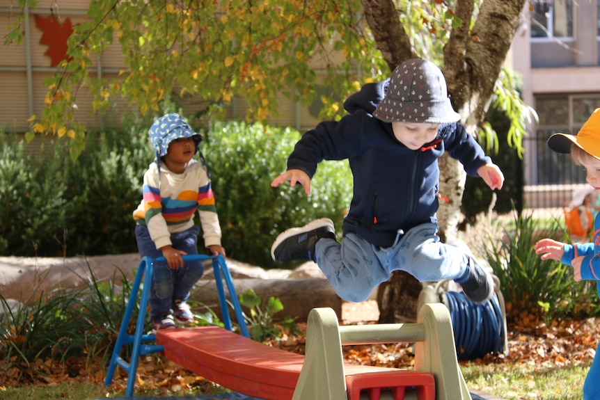 A child jumps off a slide and another climbs bars in a playground.