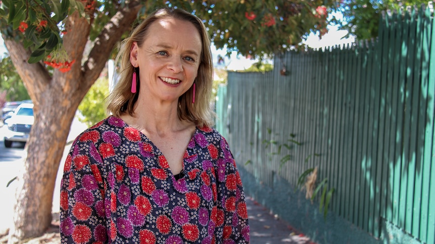 Nina Rogers stands on a footpath in front of a red flowering gum and smiles at the camera