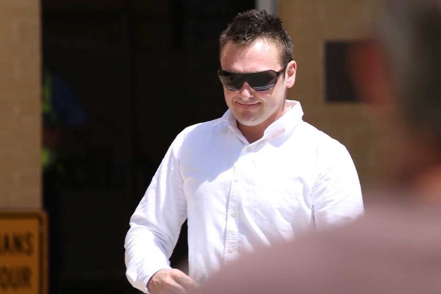 A mid shot of a man in a white shirt and sunglasses walking outside a court house.