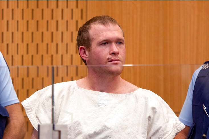 A man in a cream coloured prison uniform between two police officers