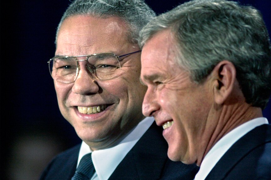 Colin Powell and George W Bush stand side by side and smile.