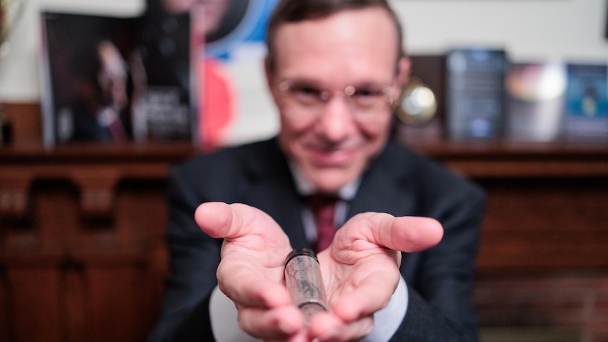 Physicist Avi Loeb holds out a tube containing meteor fragments collected from the bottom of the Pacific Ocean
