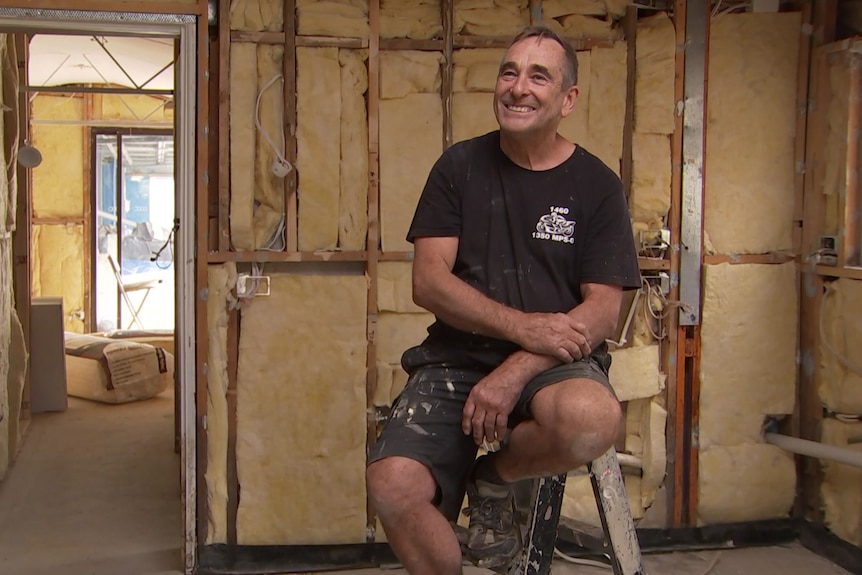 A man sits on a ladder and smiles.