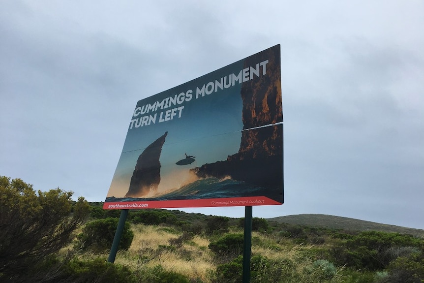 A large billboard sign of a surfer riding waves is damaged with one of its legs gone.