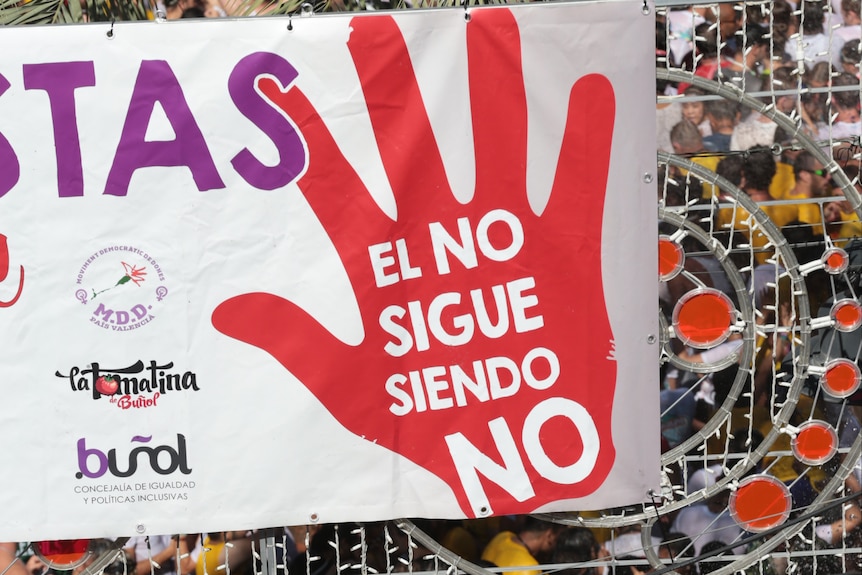 A large sign with a red handprint is hoisted above a large group of protesters