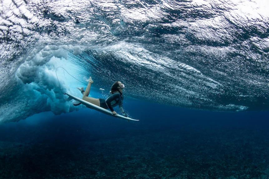 एक महिला सर्फर का चित्र उसके बोर्ड पर पानी के अंदर डूबी हुई है।