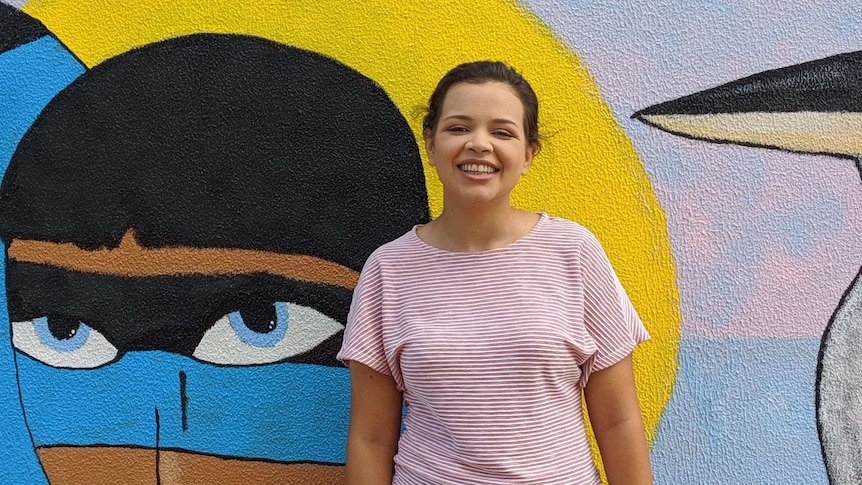 Young aboriginal woman smiling at camera in front of street art.
