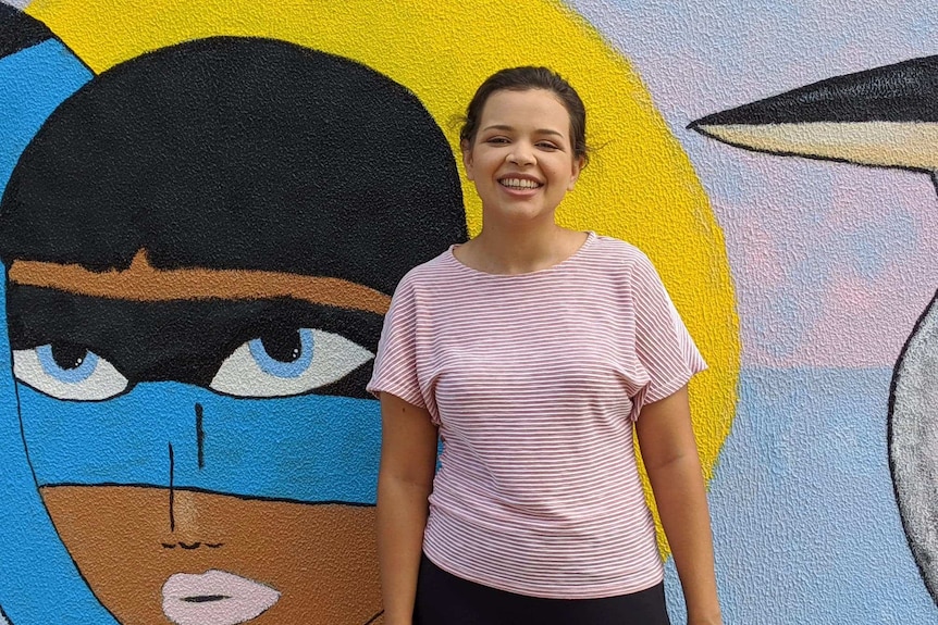 Young aboriginal woman smiling at camera in front of street art.