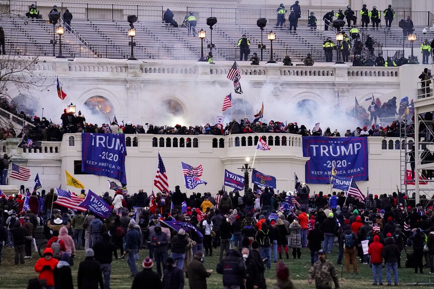 暴徒聚集在国会大厦前，手持烟雾弹旗帜。 