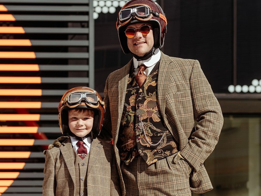 A man and his child wearing matching suits and helmets. 