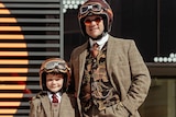 A man and his child wearing matching suits and helmets. 