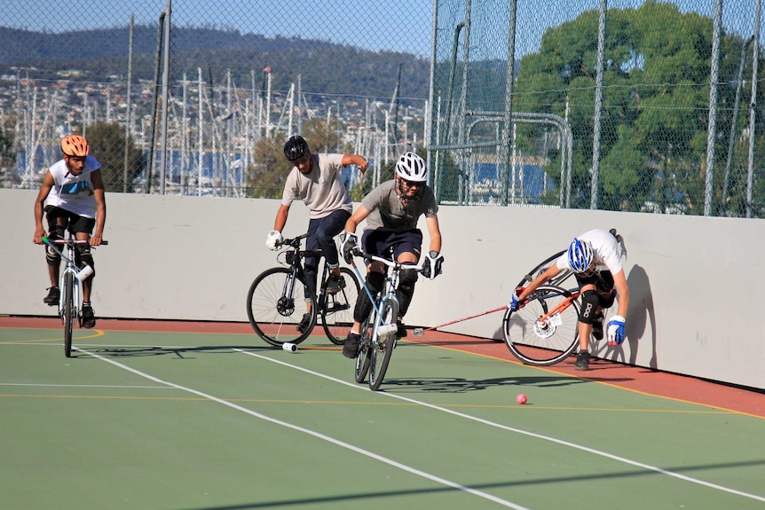 Four men on bikes on a basketball court holding mallets and wearing protective gear