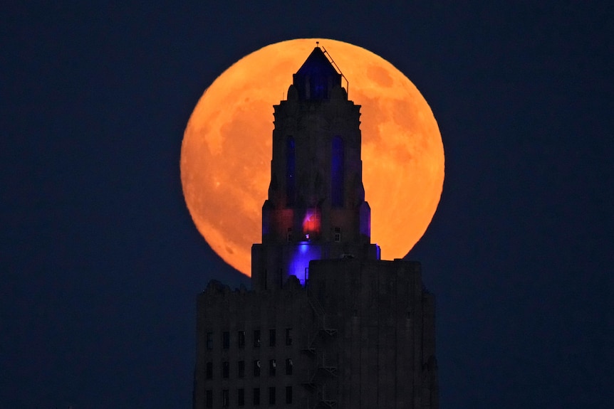 A black tower is silhouetted against a giant orange moon.