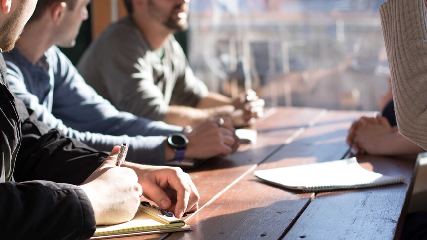 People sitting at a table with pens and paper