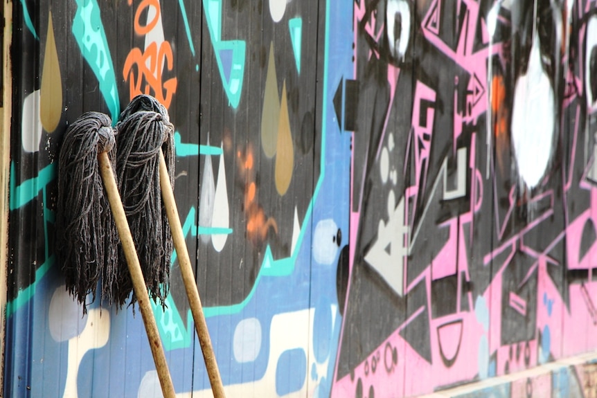 Two mops drying next to a wall with graffiti