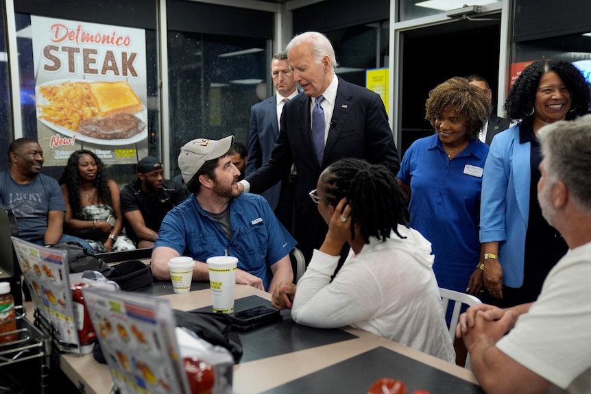 Joe Biden stands in a crowded fast food diner with multiple people looking up to him from their seats