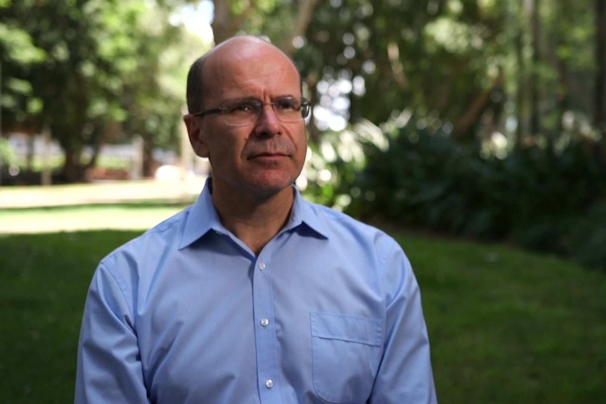 MCU of George Williams outside in front of lawn and gardens, wearing a light blue shirt.