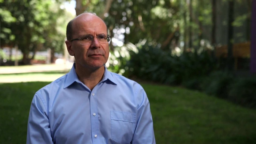 MCU of George Williams outside in front of lawn and gardens, wearing a light blue shirt.