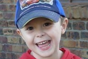 Smiling photo of four-year-old Tyrell Cobb wearing red jumper and a blue baseball cap.