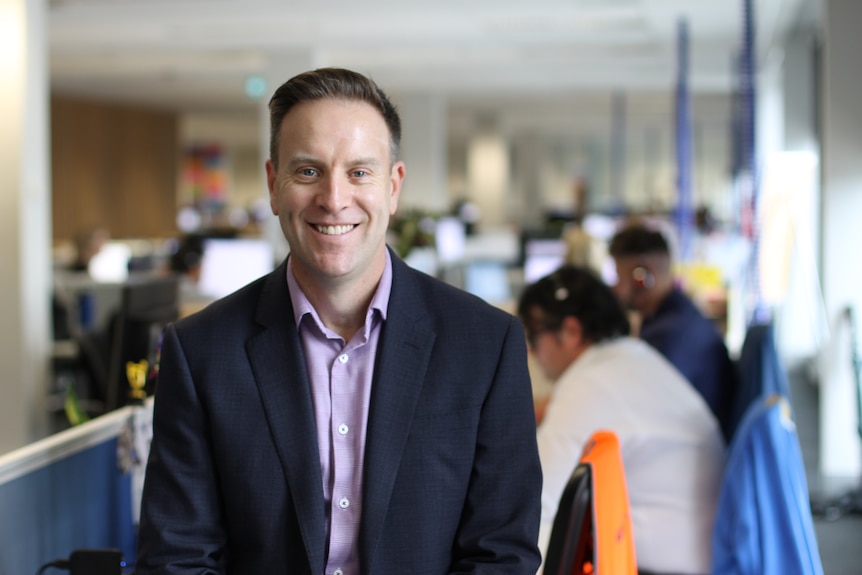 Chris kent leaning on desk in front of line of recruitment consultants in blurred background