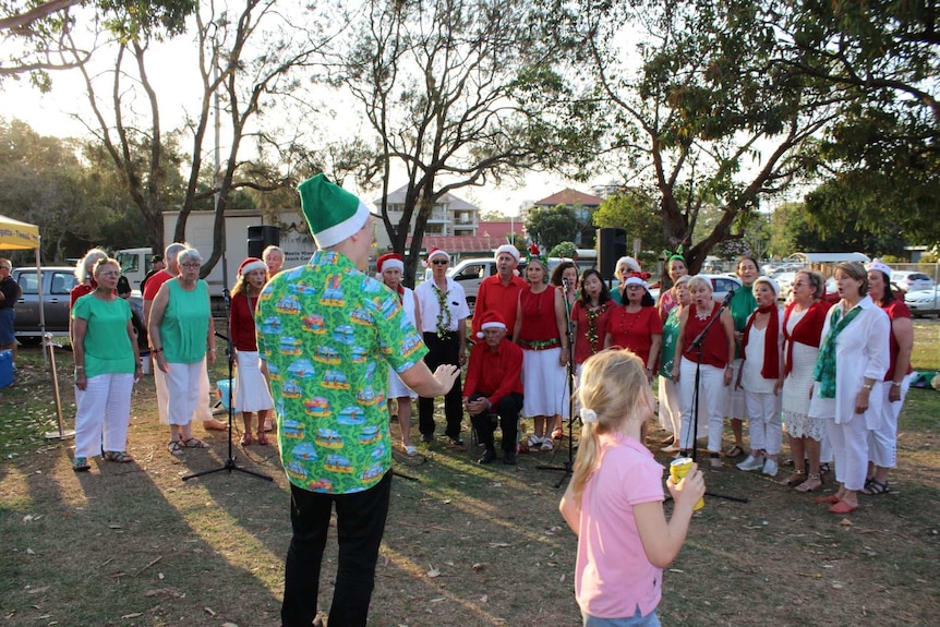 People wearing red, green and white singing Christmas carols in a park