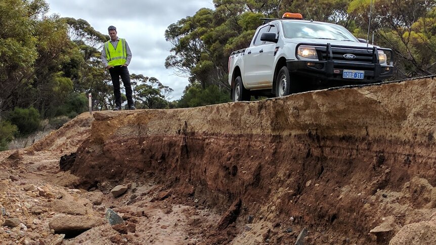 Andrew Duffield stands atop a bitumen road which has fallen away exposing the earth underneath.