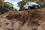 Andrew Duffield stands atop a bitumen road which has fallen away exposing the earth underneath.