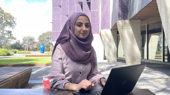 A photo of Parisa wearing a purple headscarf (hijab) with her laptop infront of her.