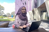 A photo of Parisa wearing a purple headscarf (hijab) with her laptop infront of her.