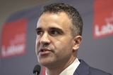 A man wearing a suit in front of Labor banners