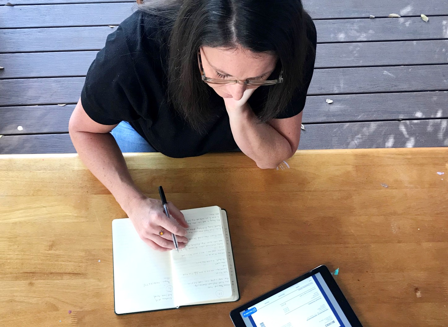 A woman sits at a table with a notebook and tablet for a story on checking bills annually to save money.