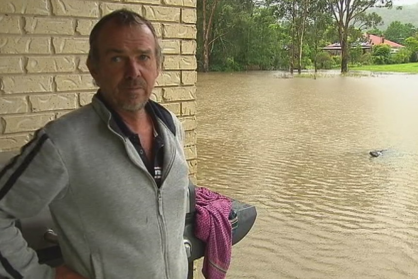 Warren Fittock stands on the edge of his house with flooding outside in Bulahdelah.
