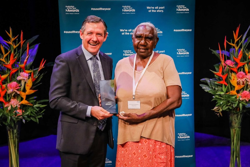 A photo of Miriam-Rose Ungunmerr Baumann holding an award and standing next to Chief Minister Michael Gunner.