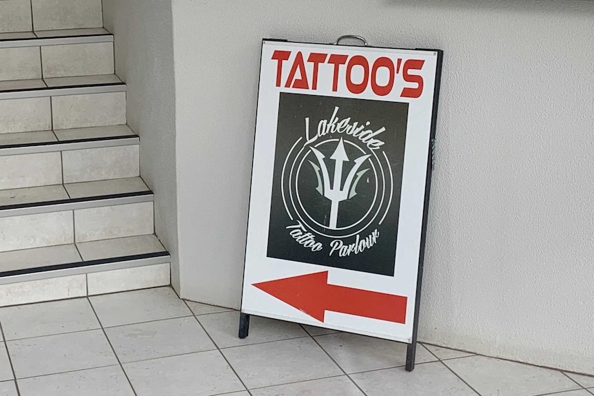 A sign advertising "tattoo's (sic.)" folded up against a wall.
