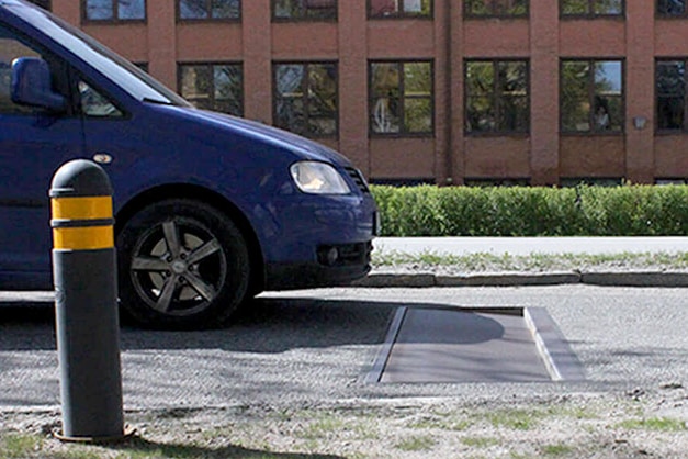 A blue car approaches a black plate in a road as seen from the side.
