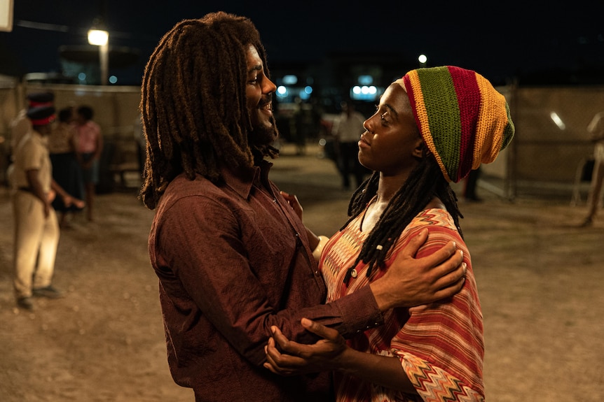 Two actors in an embrace, one with a colourful beanie on and braids, the other with Bob Marley's signature hair