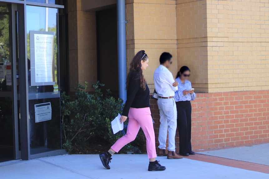 A young woman with long dark hair and pink pants leaves court